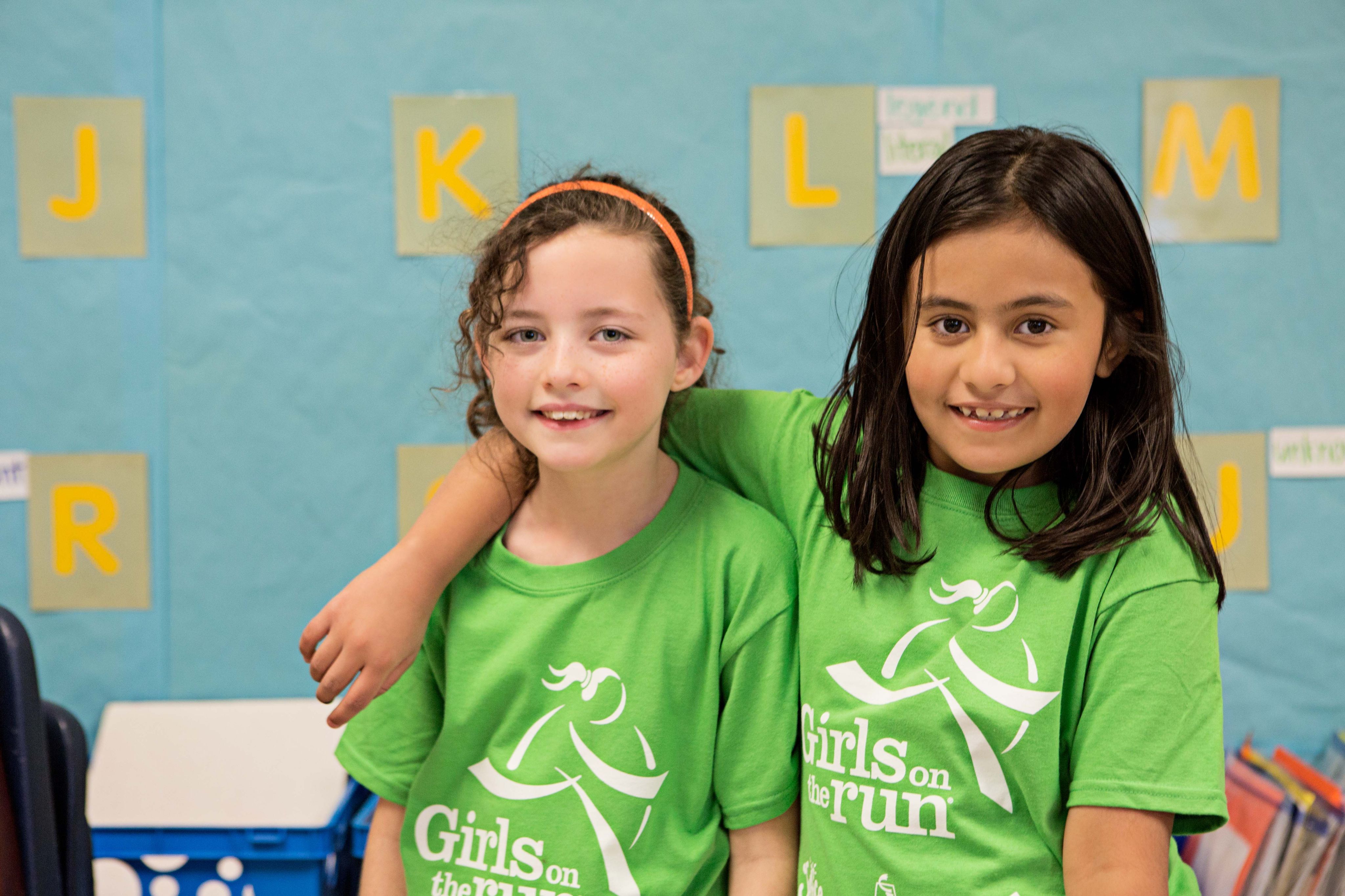 Two girls in green shirts smile at the camera. 