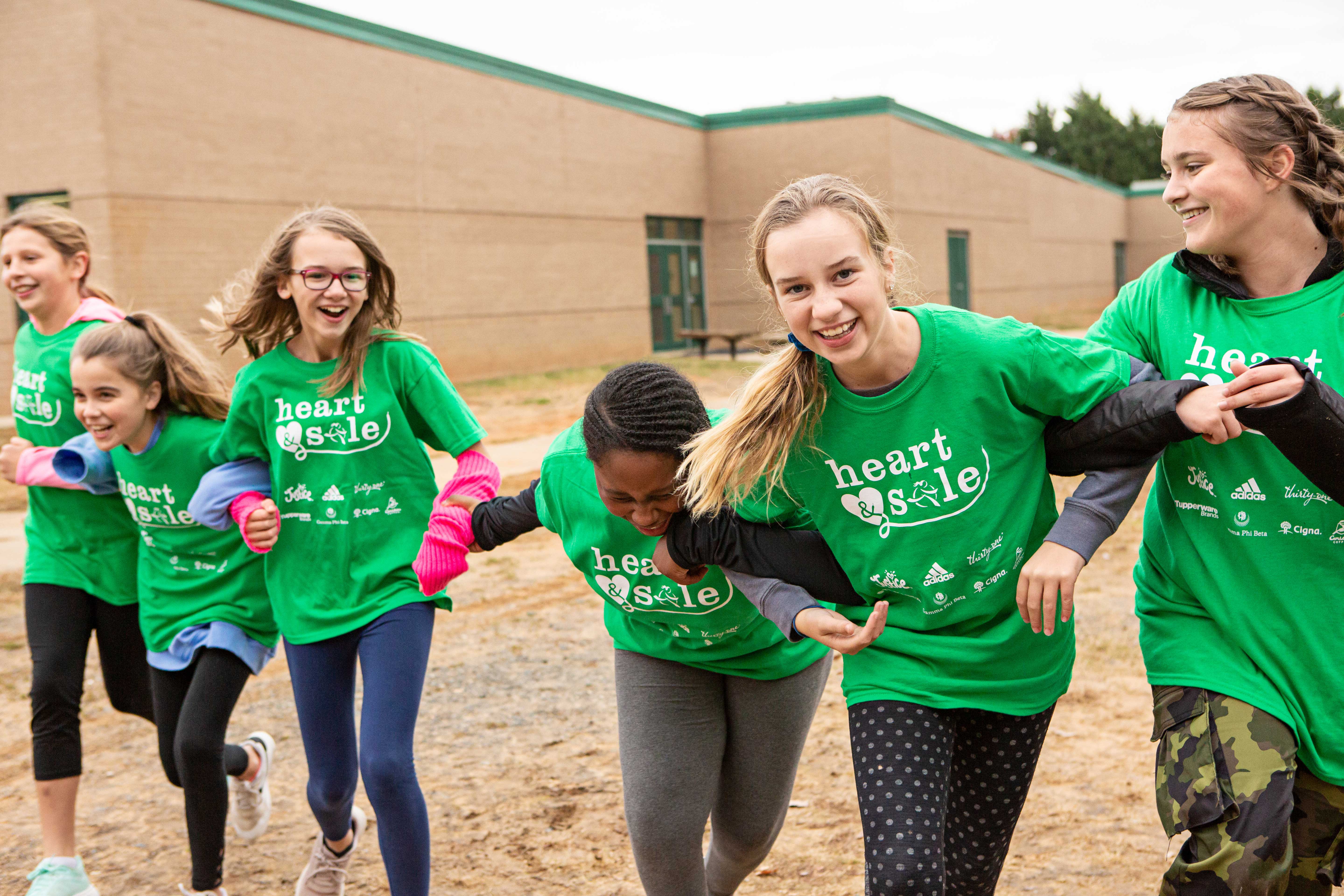 A group of middle school girls smile and laugh while standing with linked arms. 